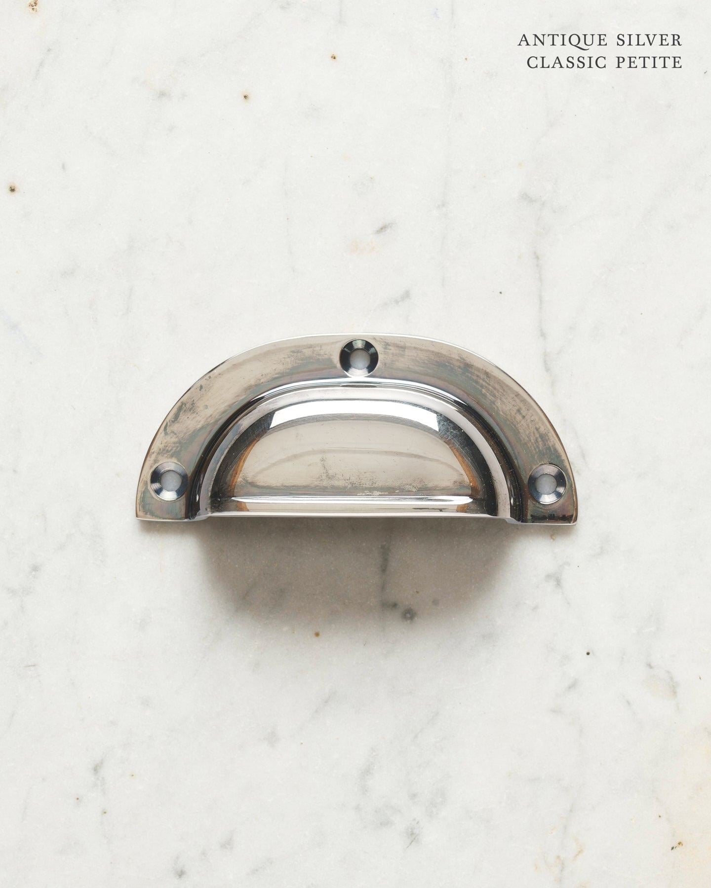 A small classic cup handle for a kitchen cupboard or drawer with a tarnished silver finish.