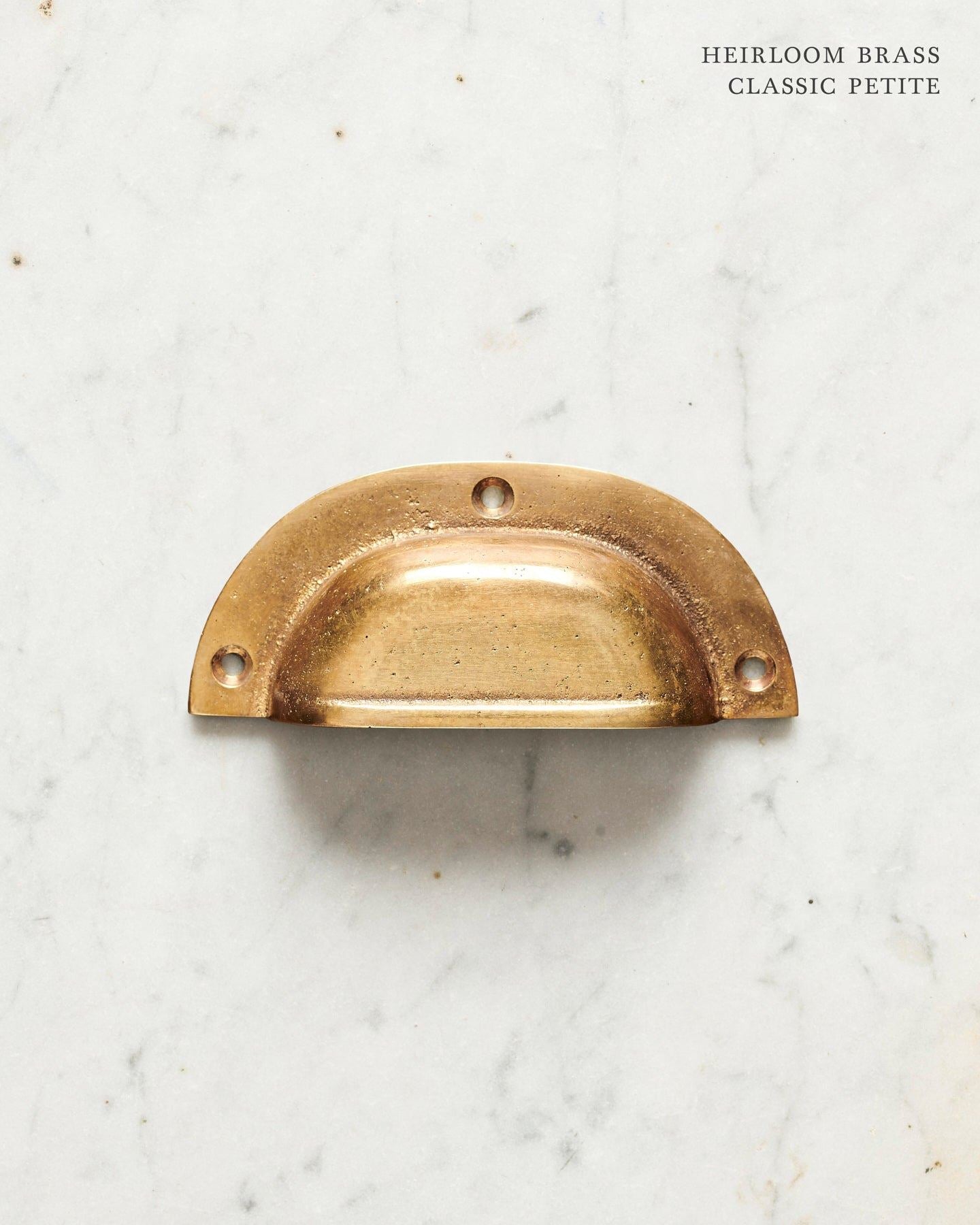 A small classic cup handle for a kitchen cupboard or drawer with a warm burnished brass finish.
