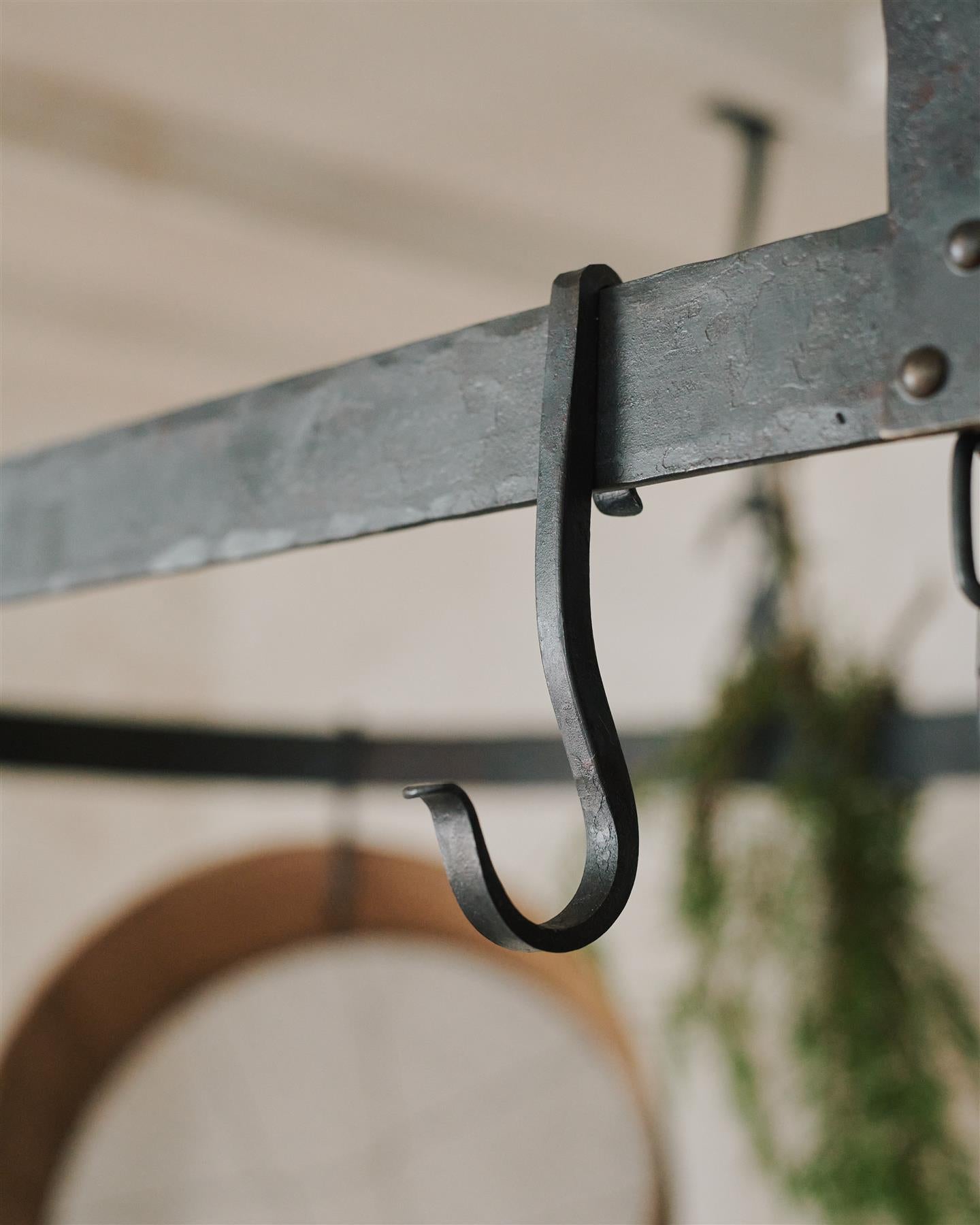A close-up view of a looped wrought iron hook hanging from the frame of a large oval-shaped pot hanger.