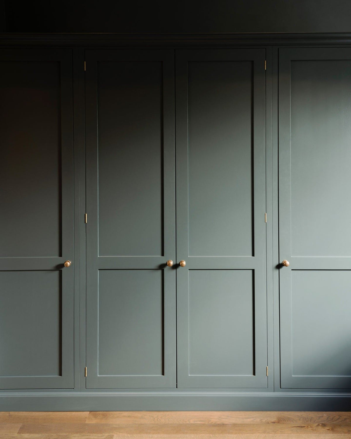 A straight-on view of dark sage green painted Shaker-style full height pantry cupboards, fitted with round doorknobs in a burnished 'Bella' brass finish.|Bella Brass Medium shown TEST