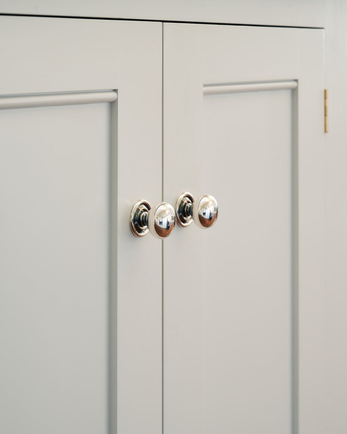 An oblique view of a pair of round doorknobs with pressed backplates in a tarnished silver finish, fitted to white painted Georgian-style kitchen cupboard doors.| Medium shown TEST