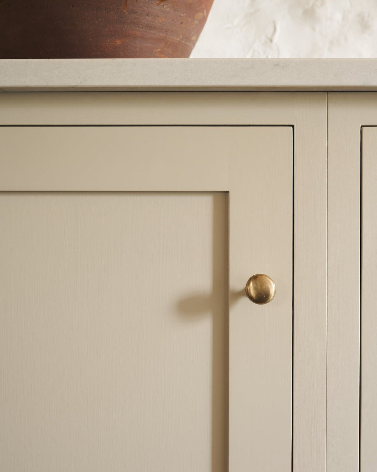 A straight-on view of a classic knob in an aged brass finish, fitted to a mushroom painted cupboard door.|Medium shown TEST