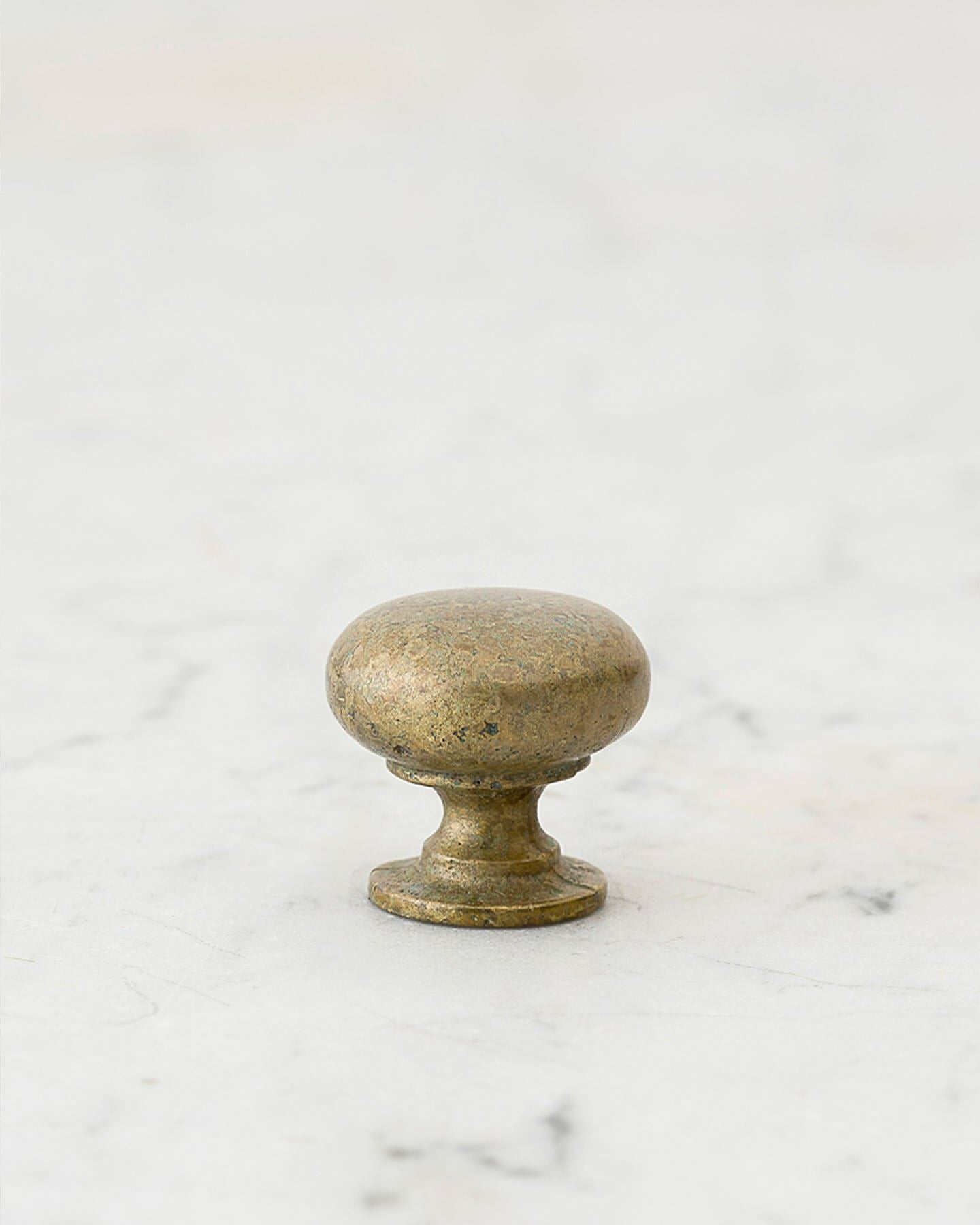 A 'Petite' classic knob for a kitchen cupboard or drawer with an aged verdigris brass finish and unique dented textures as if was made by an artisan blacksmith centuries ago.