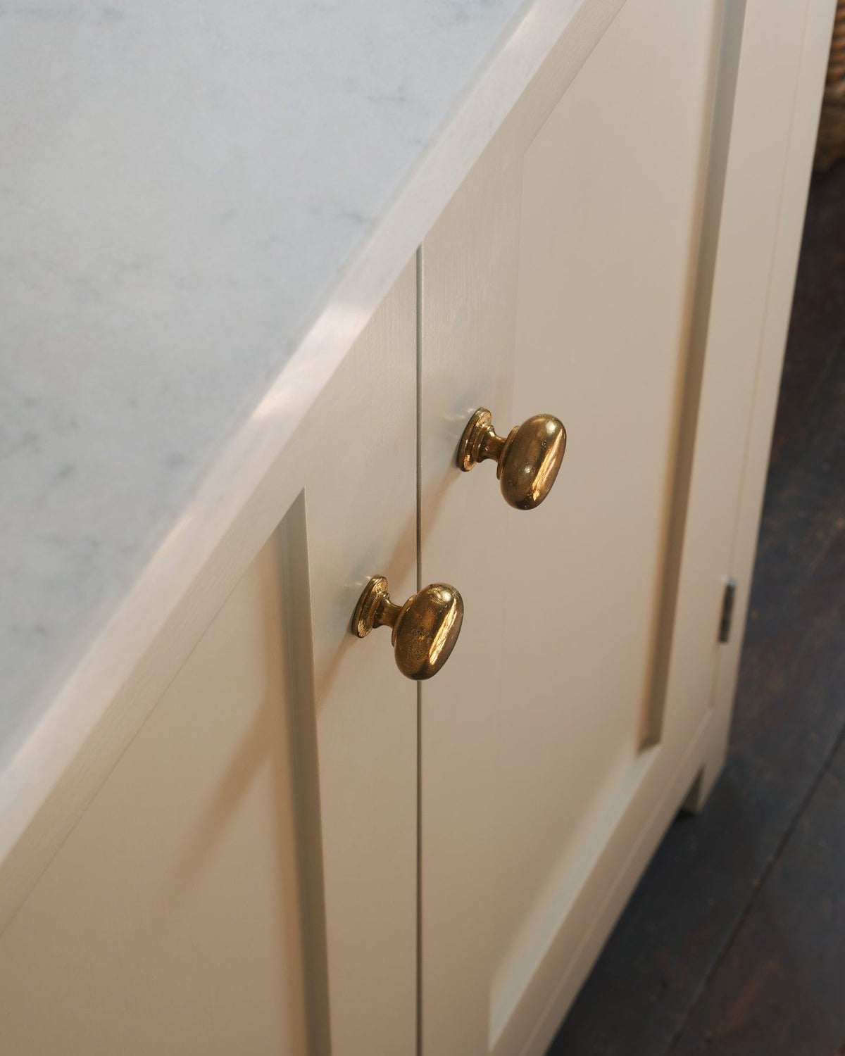 A close-up oblique view of a pair of classic knobs in a warm burnished brass finish, fitted to a mushroom painted Shaker-style kitchen cupboard.|Heirloom Brass Medium shown TEST