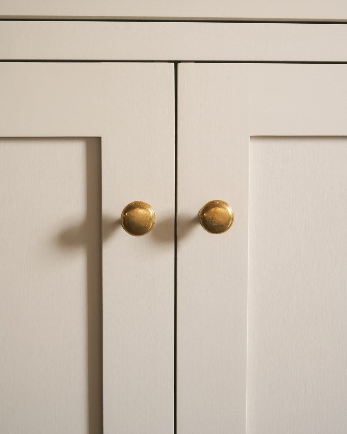 A straight-on view of a pair of classic knobs in a warm burnished brass finish, fitted to a mushroom painted Shaker-style kitchen cupboard.|Medium shown TEST