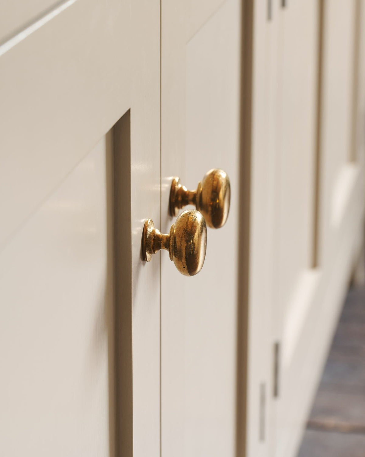 A close-up profile view of a pair of classic knobs in a warm burnished brass finish, fitted to a mushroom painted Shaker-style kitchen cupboard.|Heirloom Brass Medium shown TEST