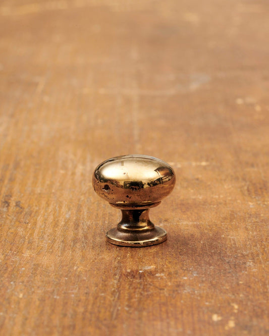 A 'Petite' classic knob for a kitchen cupboard or drawer with a warm burnished brass finish and unique dented textures as if was made by an artisan blacksmith centuries ago.