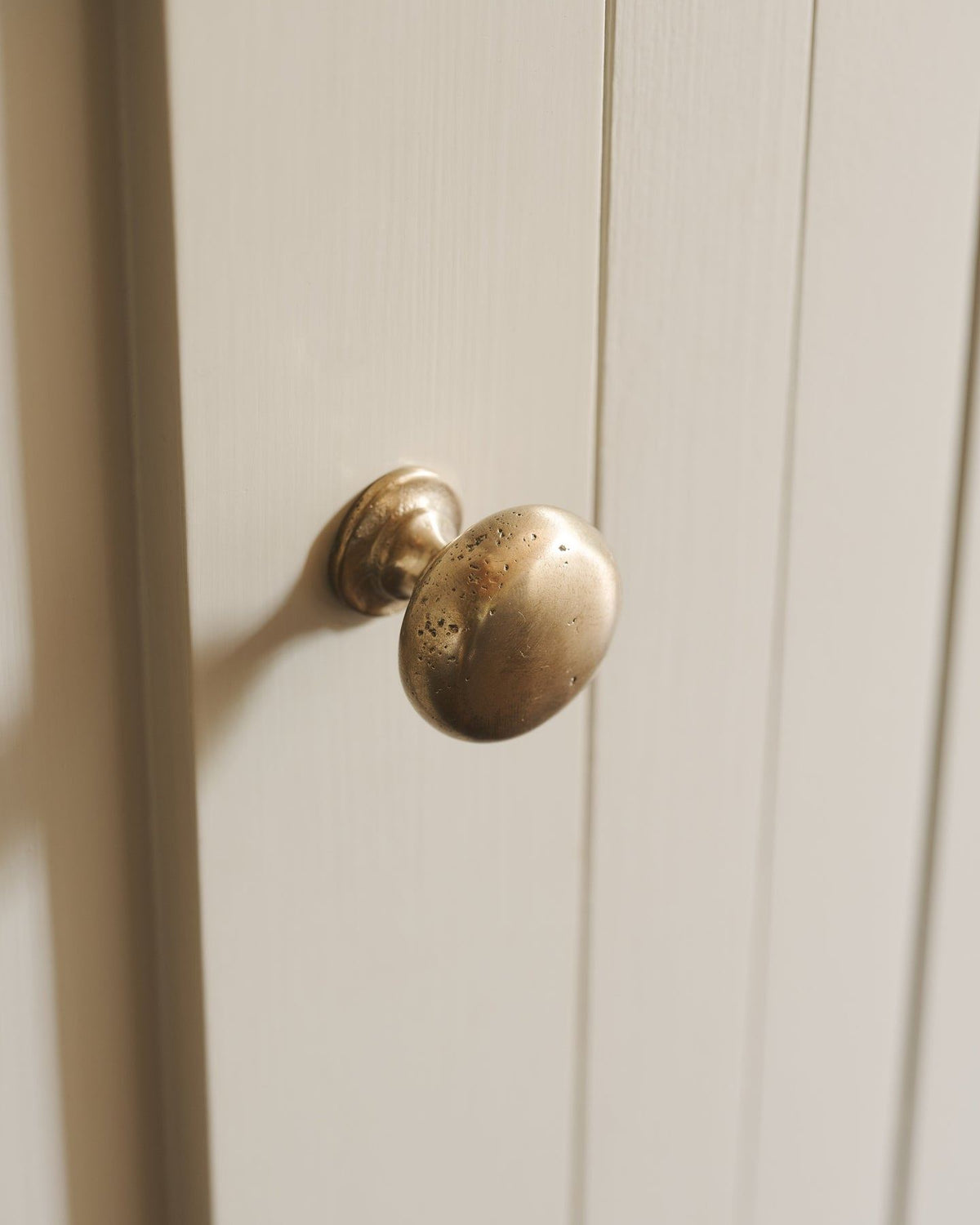 A close-up oblique view of a classic knob in an aged brass finish, fitted to a mushroom painted cupboard door. TEST
