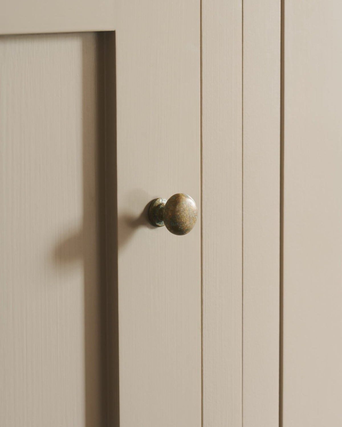 An oblique view of a classic knob in an aged verdrigris brass finish, fitted to a mushroom painted cupboard door. TEST