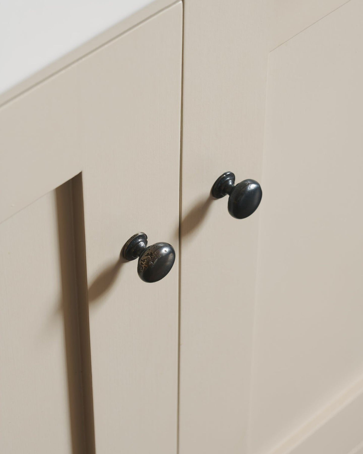 An oblique view of a pair of classic knobs in a dark oxidised bronze finish, fitted to a mushroom painted Shaker-style kitchen cupboard.|Medium shown TEST