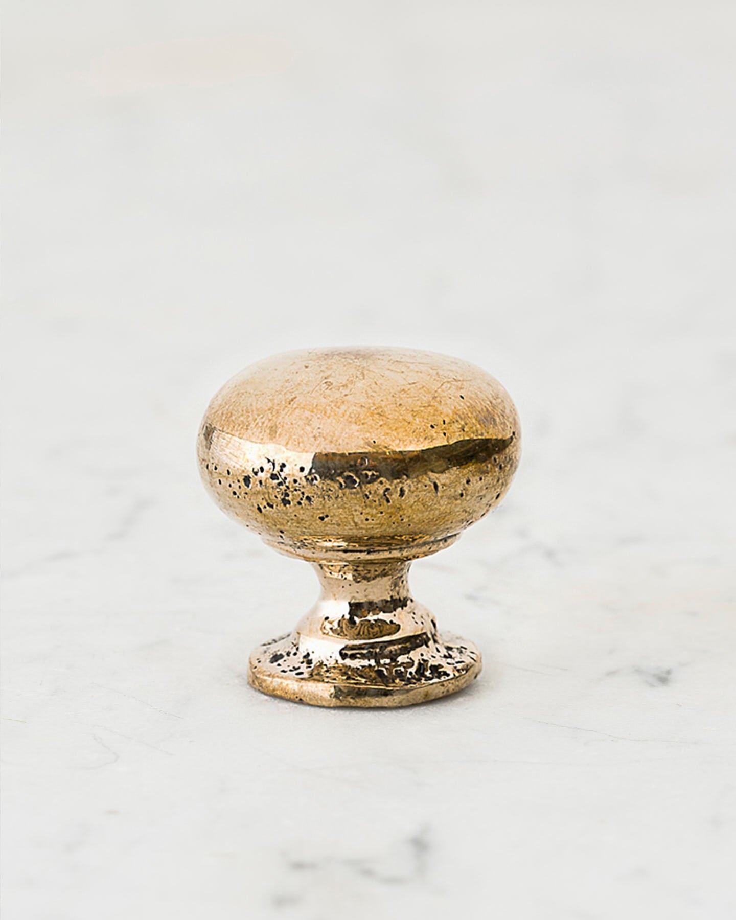 A 'Medium' classic knob for a kitchen cupboard or drawer with a bright polished bronze finish and unique dented textures that makes it look like a beloved, well aged bronze from centuries ago.