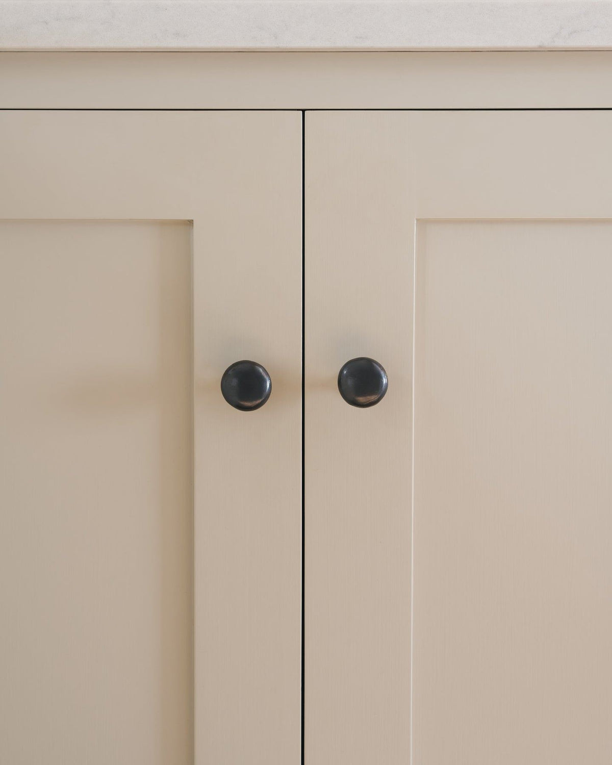 A straight-on view of a pair of classic knobs in a dark oxidised bronze finish, fitted to a mushroom painted Shaker-style kitchen cupboard.|Medium shown TEST