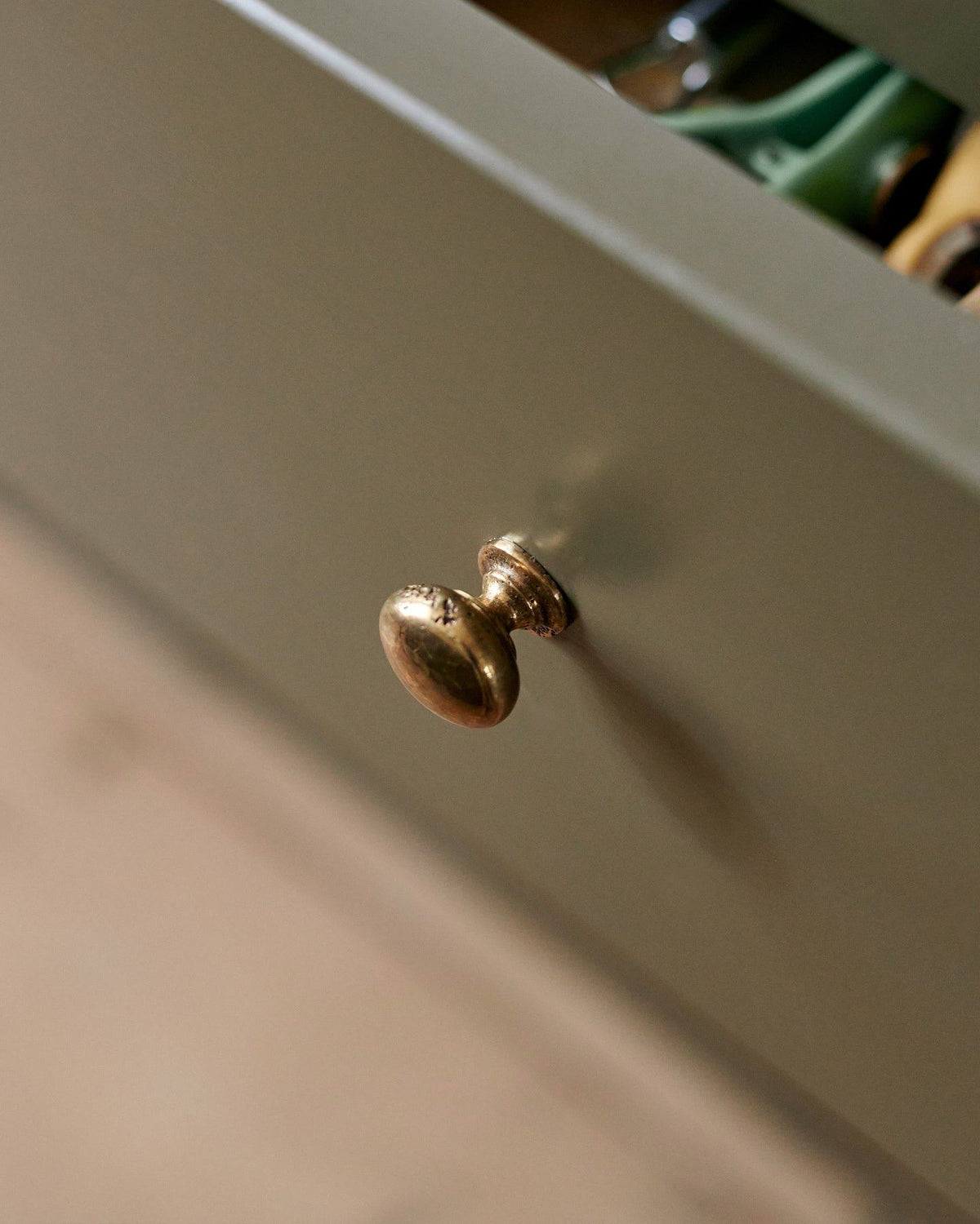 A close-up oblique view of a classic knob in a bright polished bronze finish, fitted to a mossy green painted drawer front.|Medium shown TEST