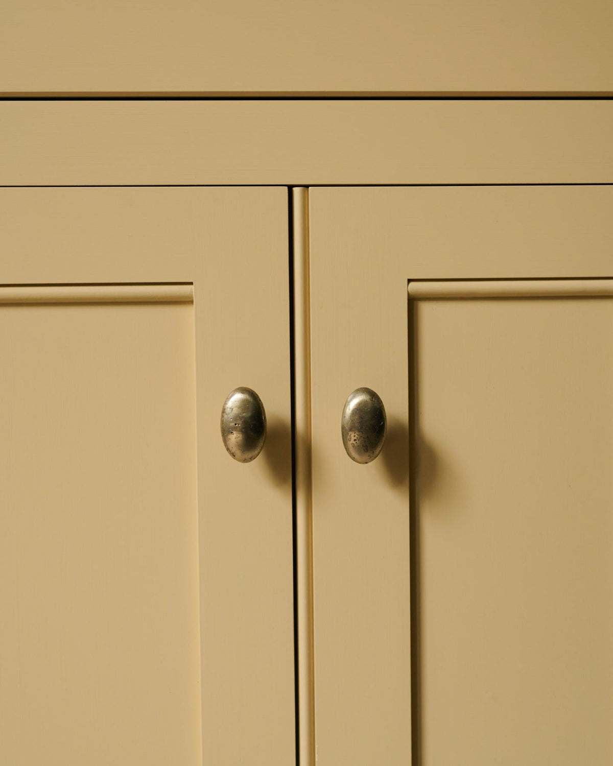 A straight-on view of a pair of oval-shaped knobs in an aged brass finish, fitted to a yellow painted Georgian-style kitchen cupboard. | Aged Brass Large shown TEST