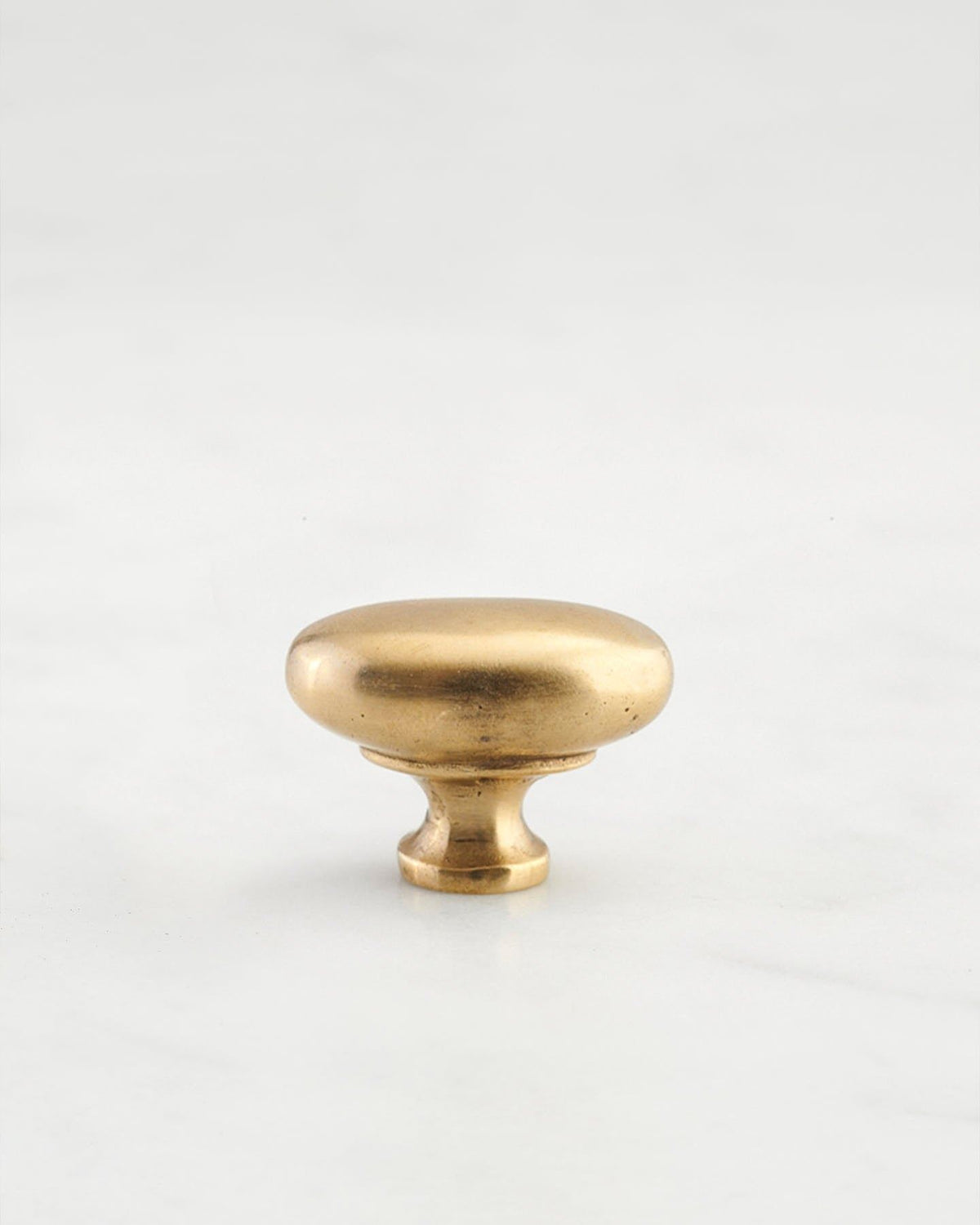 A 'Petite' oval-shaped knob for a kitchen cupboard or drawer with an aged brass finish and unique dented textures that makes it look like a beloved, well aged brass from centuries ago. TEST