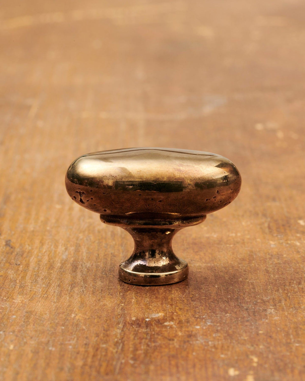 A 'Medium' oval-shaped knob for a kitchen cupboard or drawer with a warm burnished brass finish and unique dented textures as if was made by an artisan blacksmith centuries ago. TEST