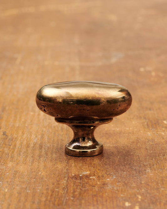 A 'Medium' oval-shaped knob for a kitchen cupboard or drawer with a warm burnished brass finish and unique dented textures as if was made by an artisan blacksmith centuries ago.