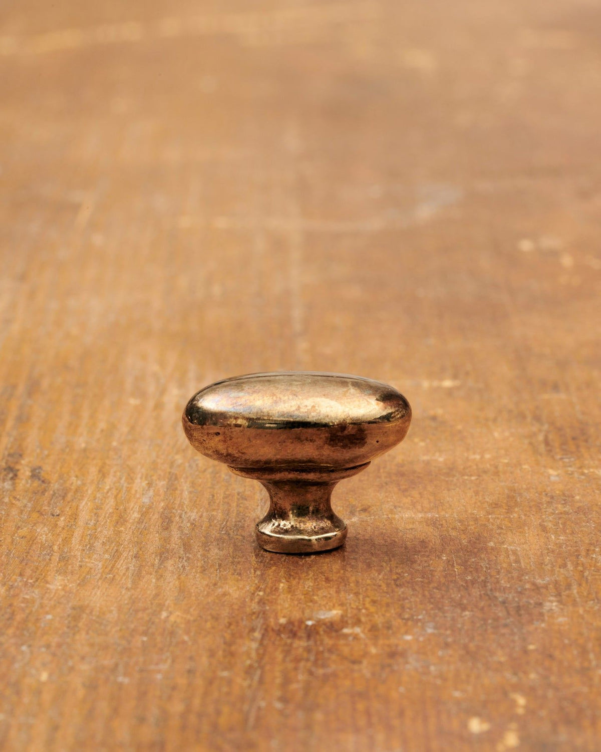 A 'Petite' oval-shaped knob for a kitchen cupboard or drawer with a warm burnished brass finish and unique dented textures as if was made by an artisan blacksmith centuries ago. TEST