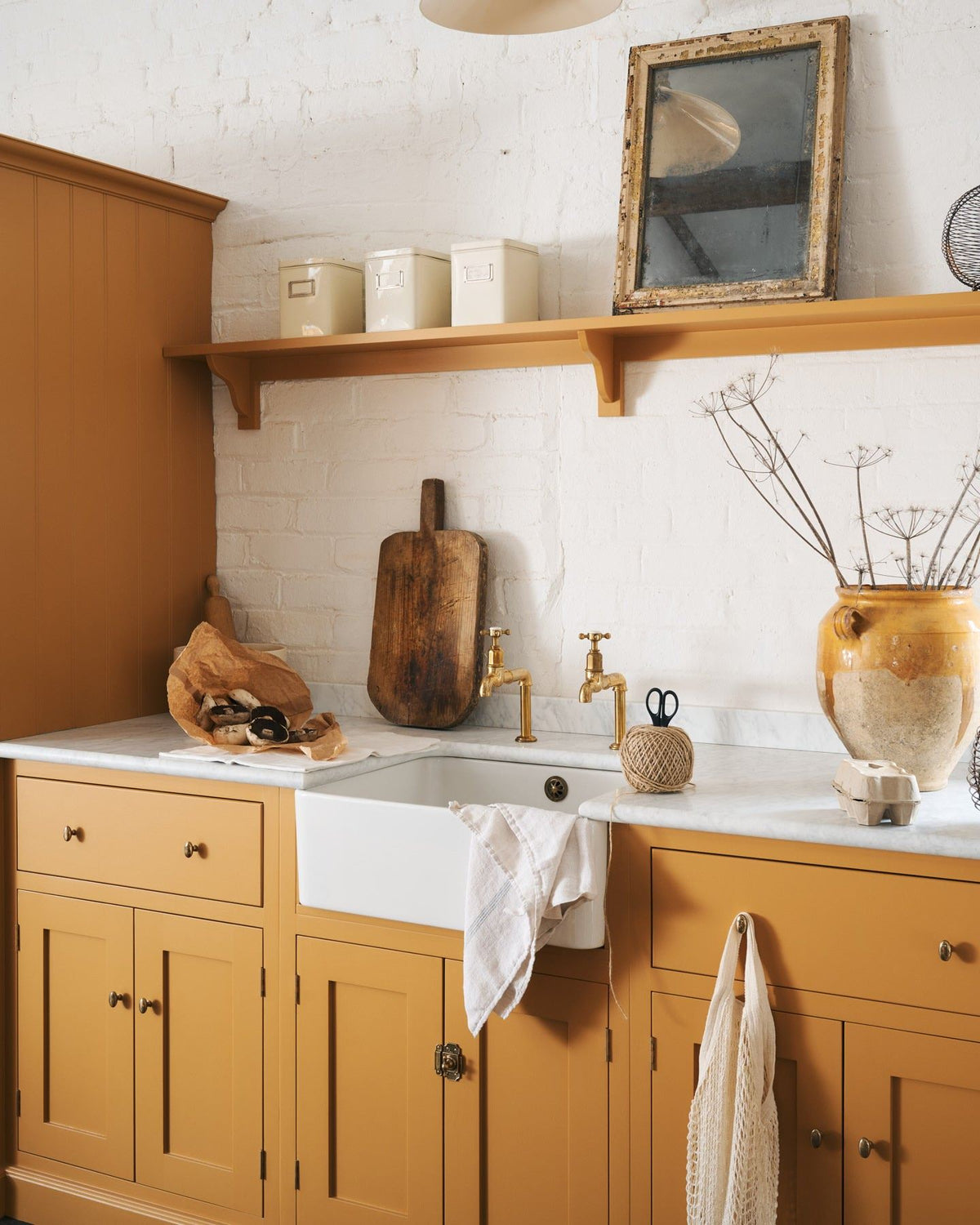 An oblique view of a yellow painted Shaker-style kitchen sink cupboard with small oval-shaped knobs in a warm burnished brass finish. TEST