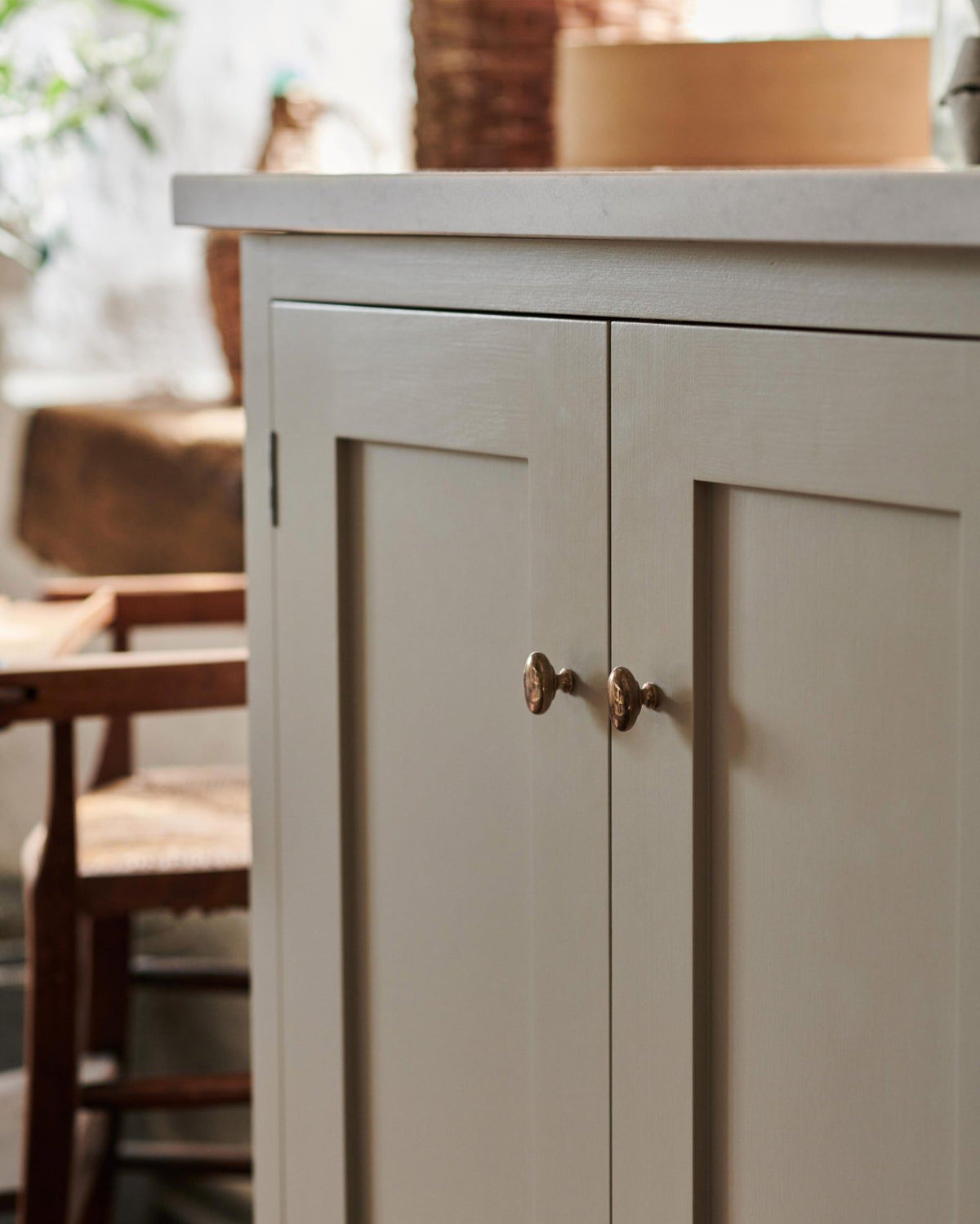 An oblique view of a pair of oval-shaped knobs in a warm burnished brass finish, fitted to a mushroom painted Shaker-style kitchen cupboard.| Heirloom Brass Small shown TEST