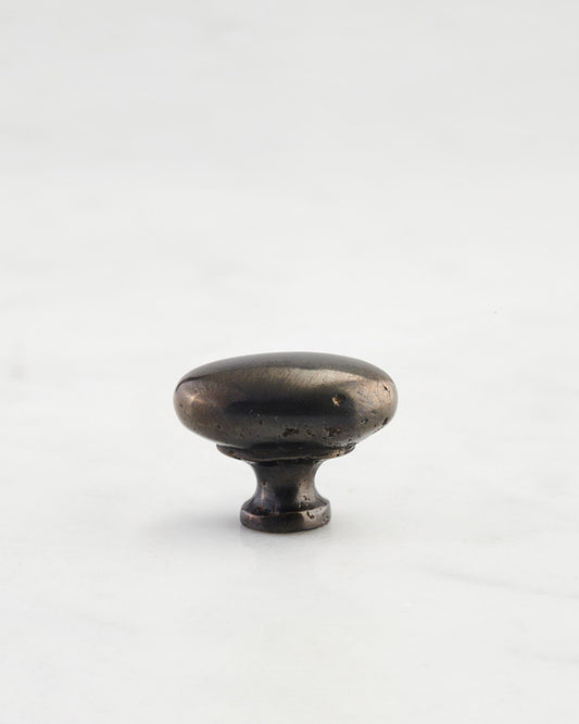 A 'Petite' oval-shaped knob for a kitchen cupboard or drawer with a dark oxidised bronze finish that makes it look like a beloved, well aged brass from centuries ago.