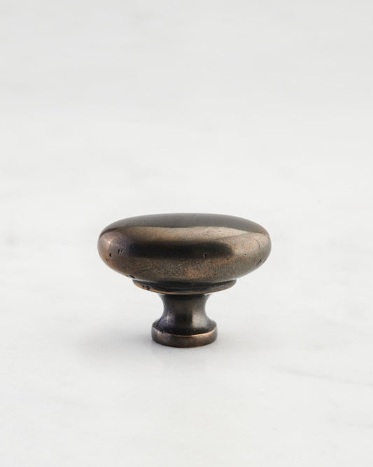 A 'Small' oval-shaped knob for a kitchen cupboard or drawer with a dark oxidised bronze finish and unique dented textures as if was made by an artisan blacksmith centuries ago.