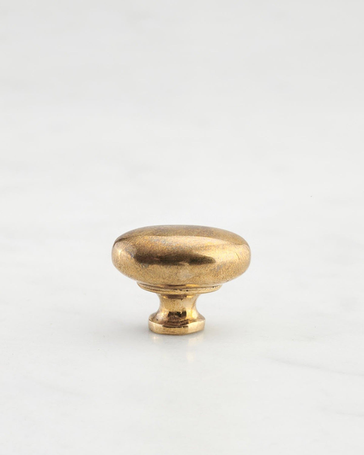 A 'Petite' oval-shaped knob for a kitchen cupboard or drawer with a bright polished bronze finish and unique dented textures that makes it look like a beloved, well aged bronze from centuries ago. TEST