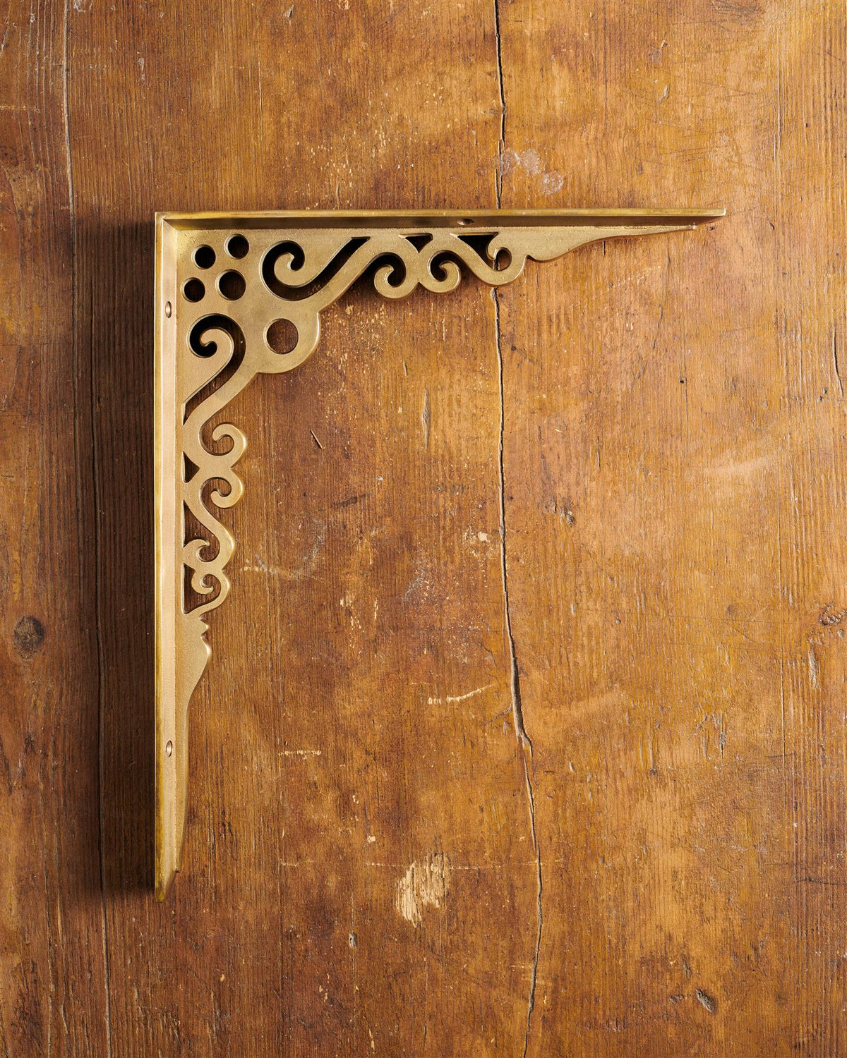 A side profile view of a large Victorian-inspired ornate shelf bracket in an aged brass finish. TEST