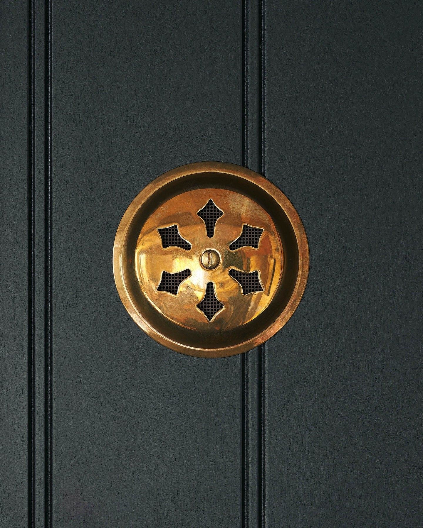 A Victorian-inspired circular brass ventilation grille with traditional decorative cutouts.