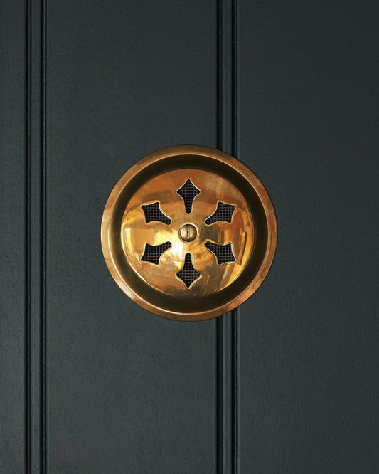 A Victorian-inspired circular brass ventilation grille with traditional decorative cutouts.