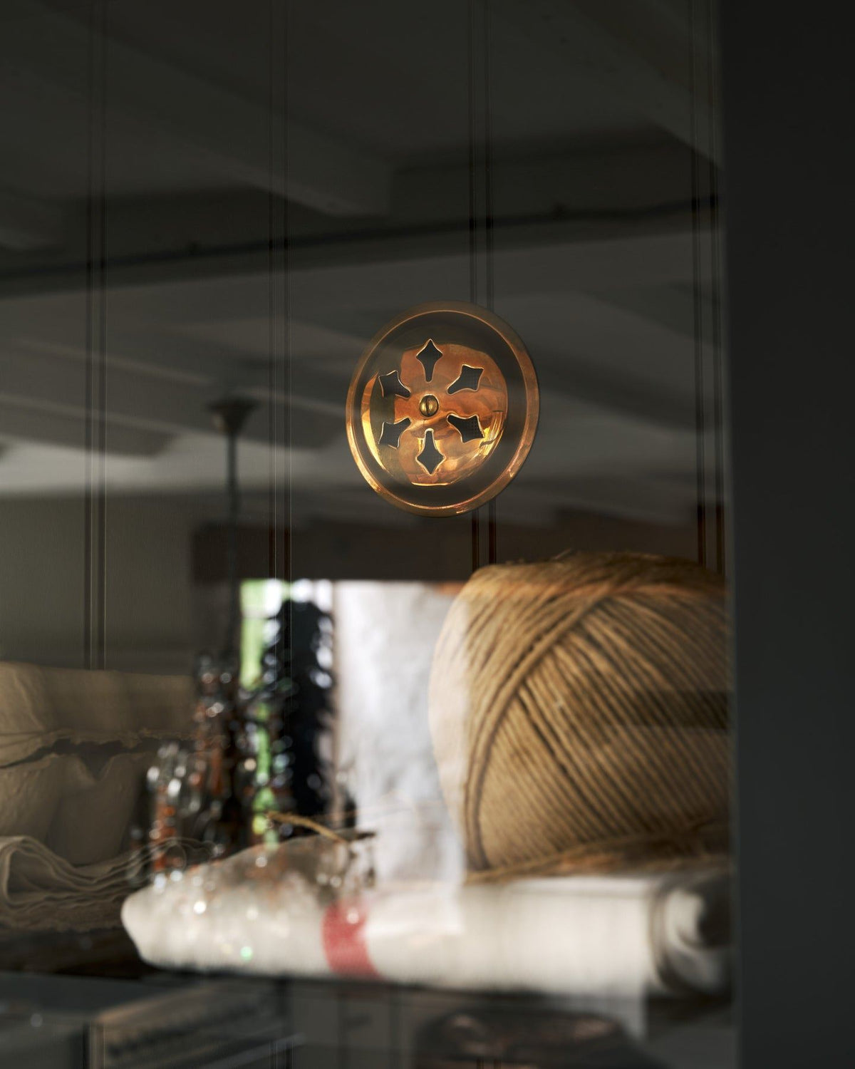 Looking through a glazed cupboard door at a Victorian-inspired circular brass ventilation grille with traditional decorative cutouts fitted to a black painted tongue and groove-style back panel. TEST
