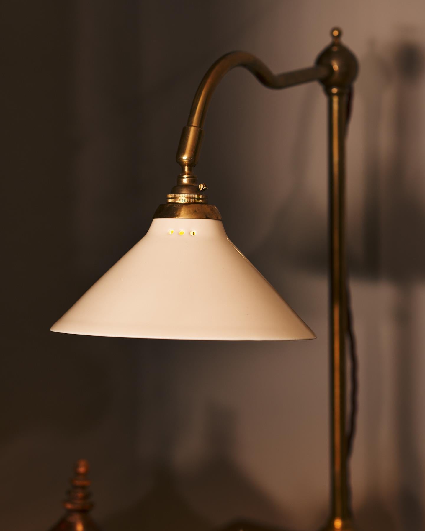 A close-up view of a small cream glazed ceramic light shade fitted to a curved brass arm with a pointed finial.