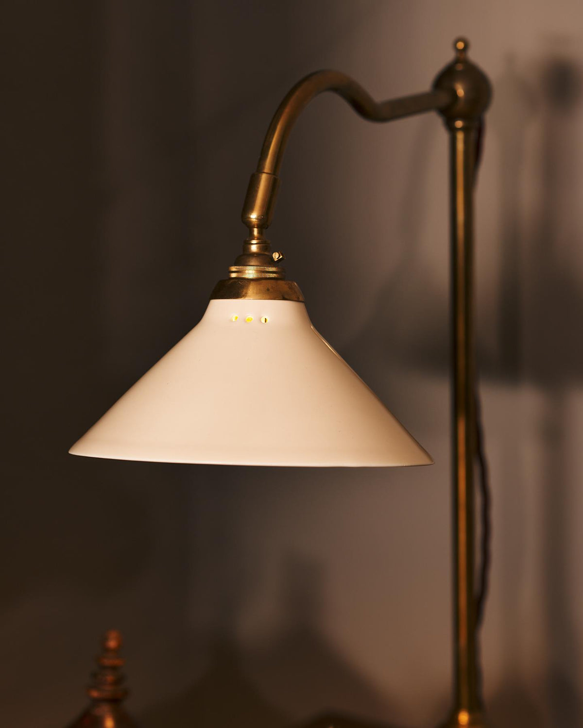 A close-up view of a small cream glazed ceramic light shade fitted to a curved brass arm with a pointed finial. TEST