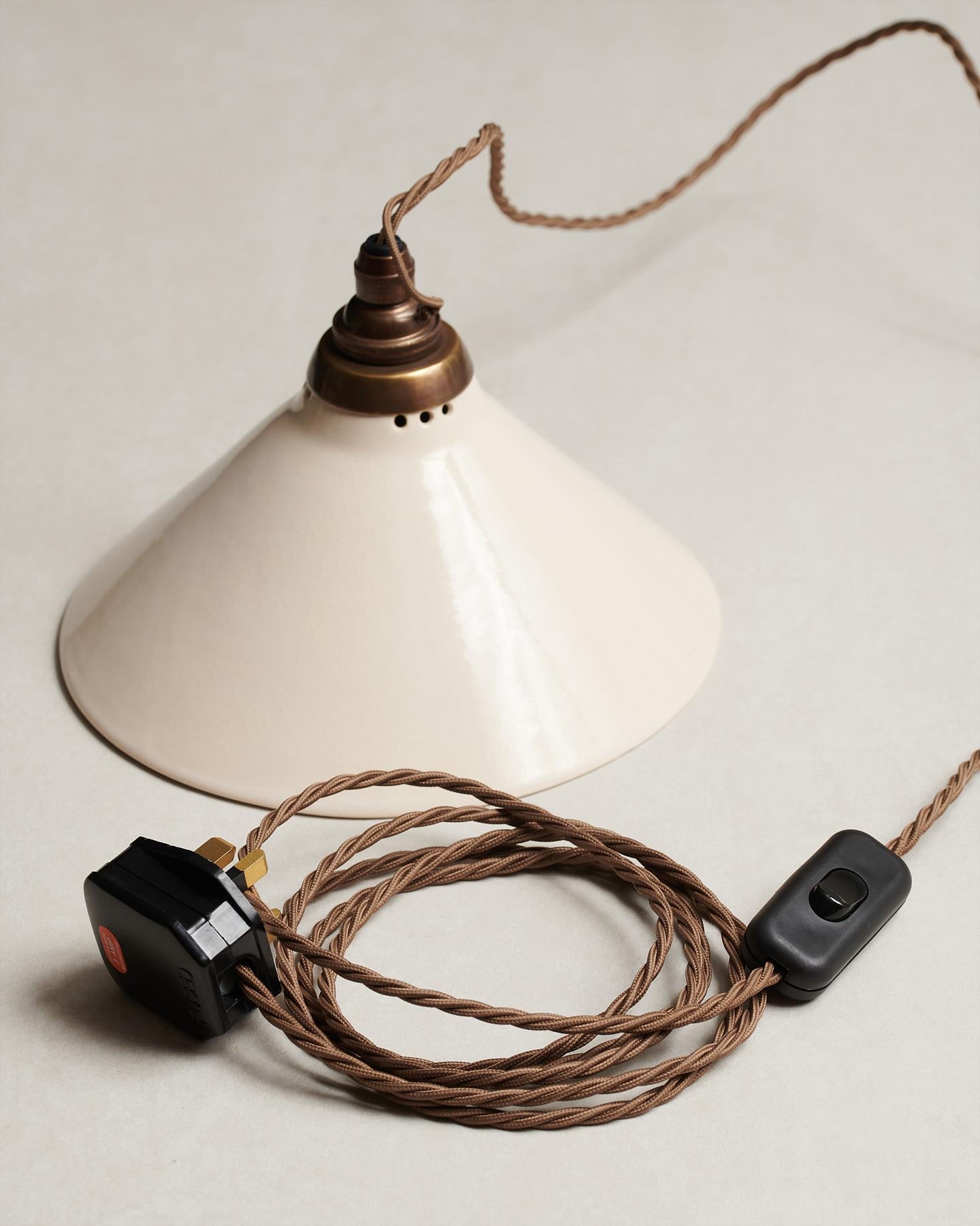 A small plug-in light with a cream glazed shade, brown twisted fabric flex cord, brass fittings and a black plastic switch and plug.