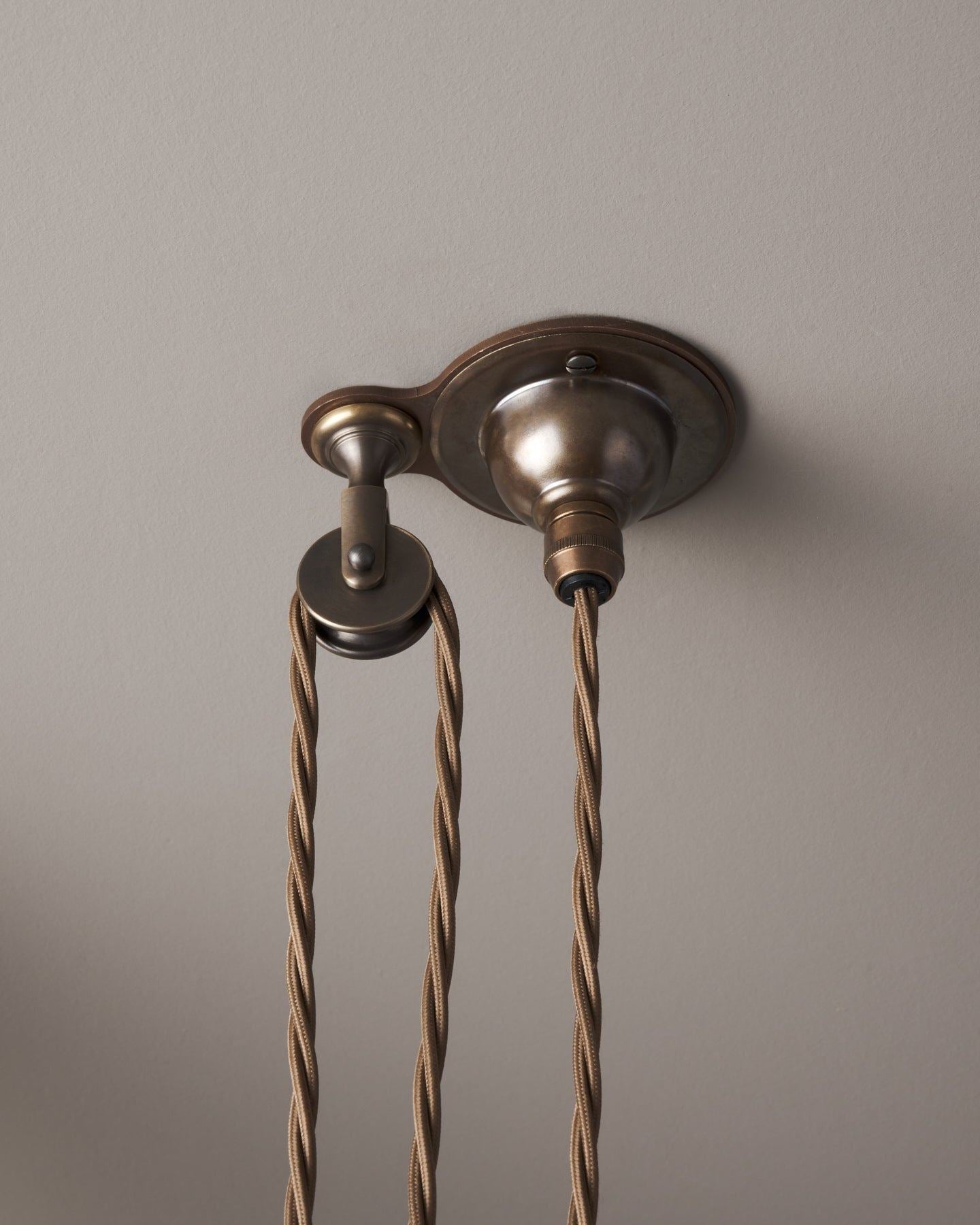 A small aged brass ceiling rose with a wheel pulley and a brown twisted fabric flex cord.