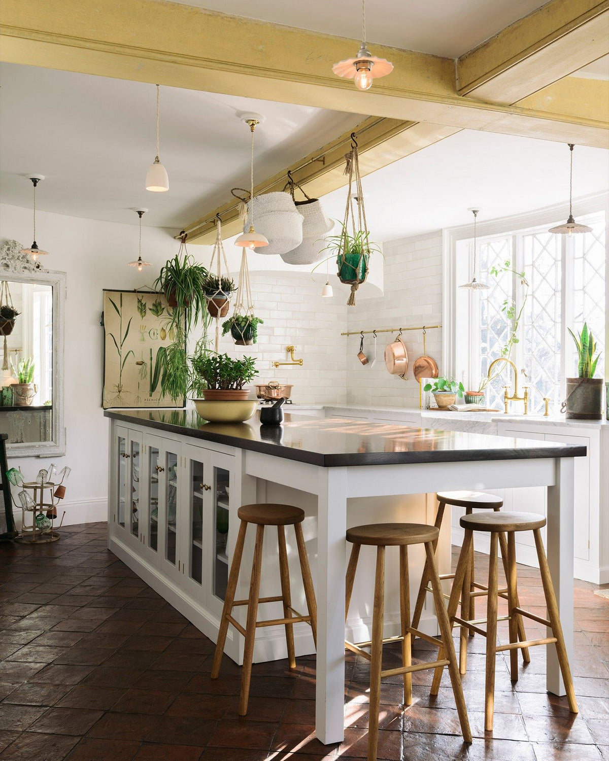 A Mediterranean-style kitchen with white painted cabinetry, white walls, terracotta flooring and an assortment of unglazed porcelain pendant lights hanging at various heights. TEST
