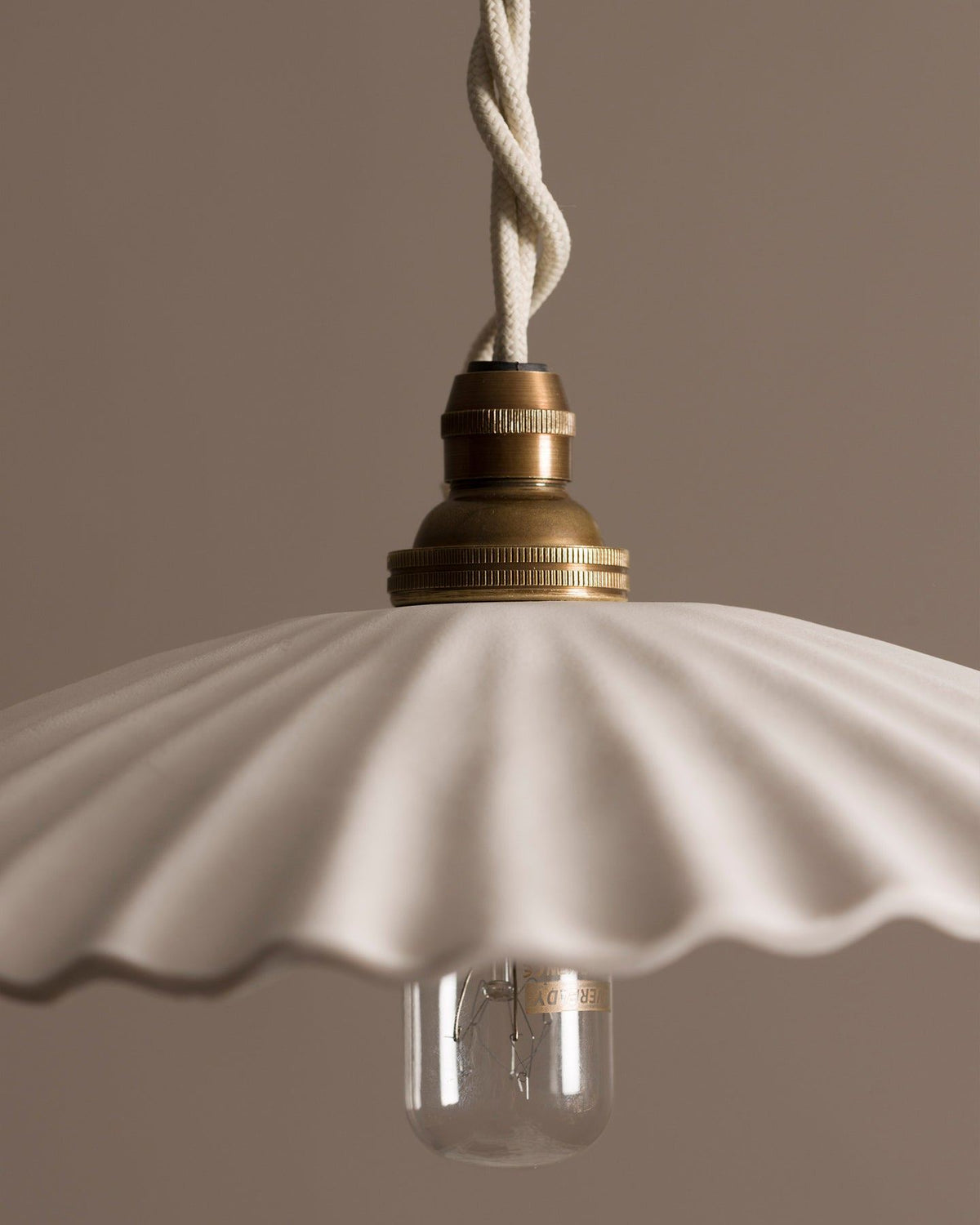 A close-up view of an unglazed porcelain pendant light with narrow pleats. TEST