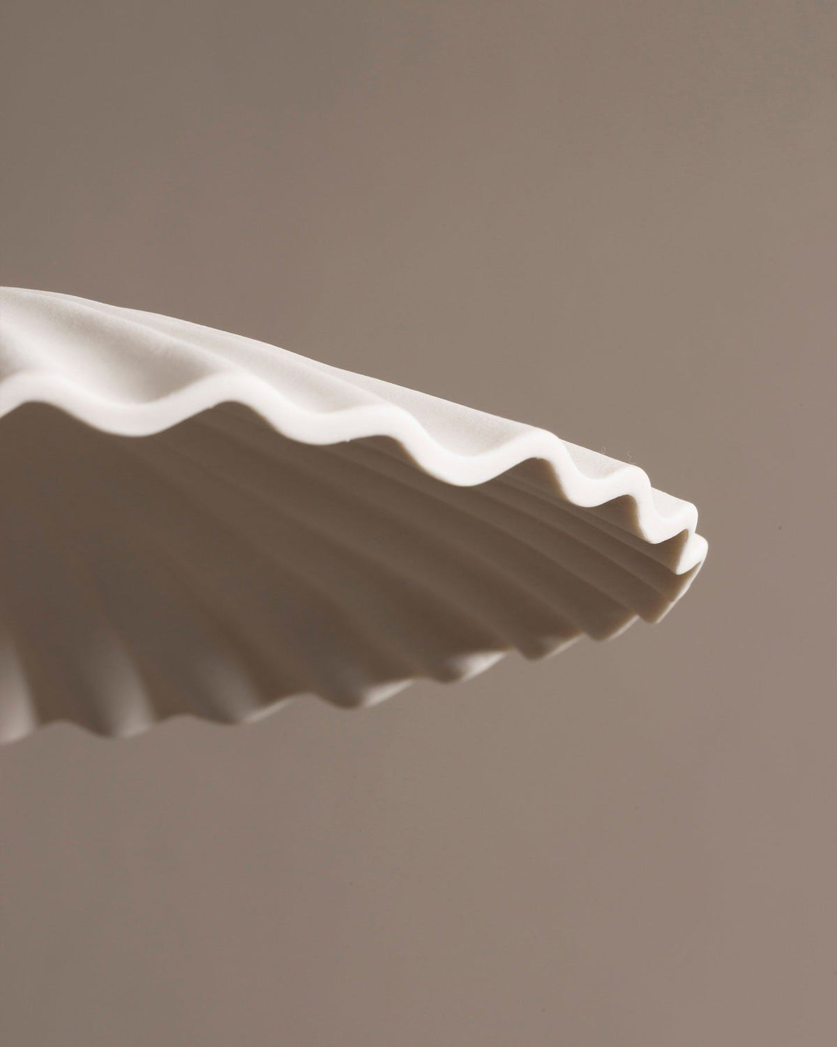 A close-up view of an unglazed porcelain pendant light with narrow pleats. TEST