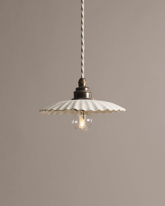 A small narrow pleat porcelain pendant light with an unglazed finish, an aged brass E27 lampholder and a white twisted fabric flex cord.