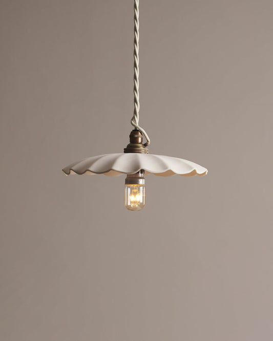 A large wide pleat porcelain pendant light with an unglazed finish, an aged brass B22 lampholder and a white twisted fabric flex cord.