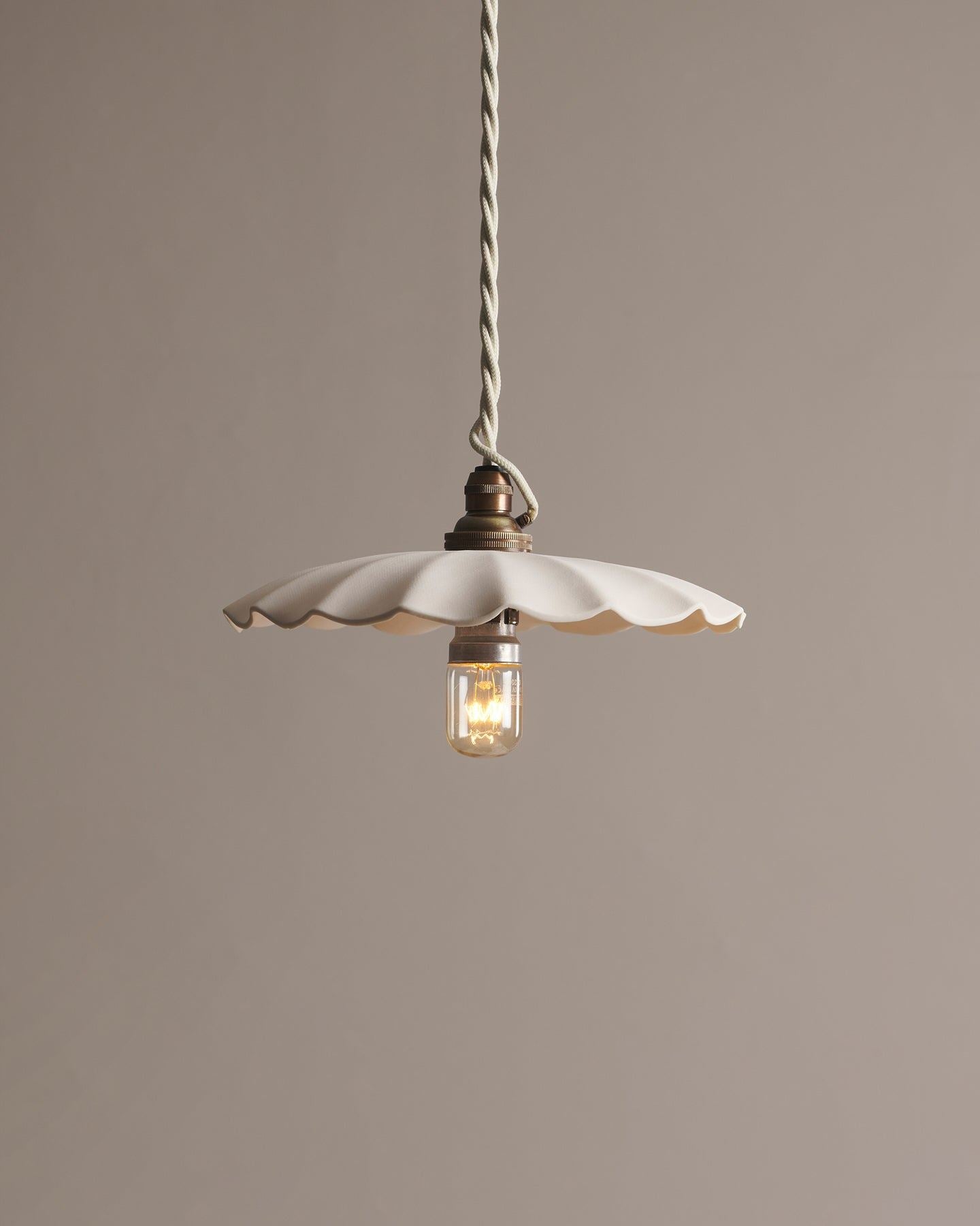 A large wide pleat porcelain pendant light with an unglazed finish, an aged brass B22 lampholder and a white twisted fabric flex cord.