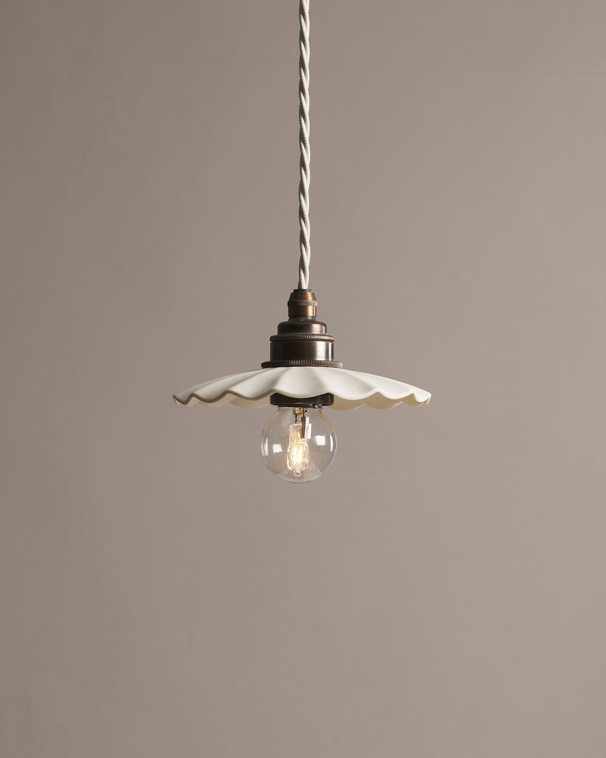 A small wide pleat porcelain pendant light with an unglazed finish, an aged brass E27 lampholder and a white twisted fabric flex cord. TEST