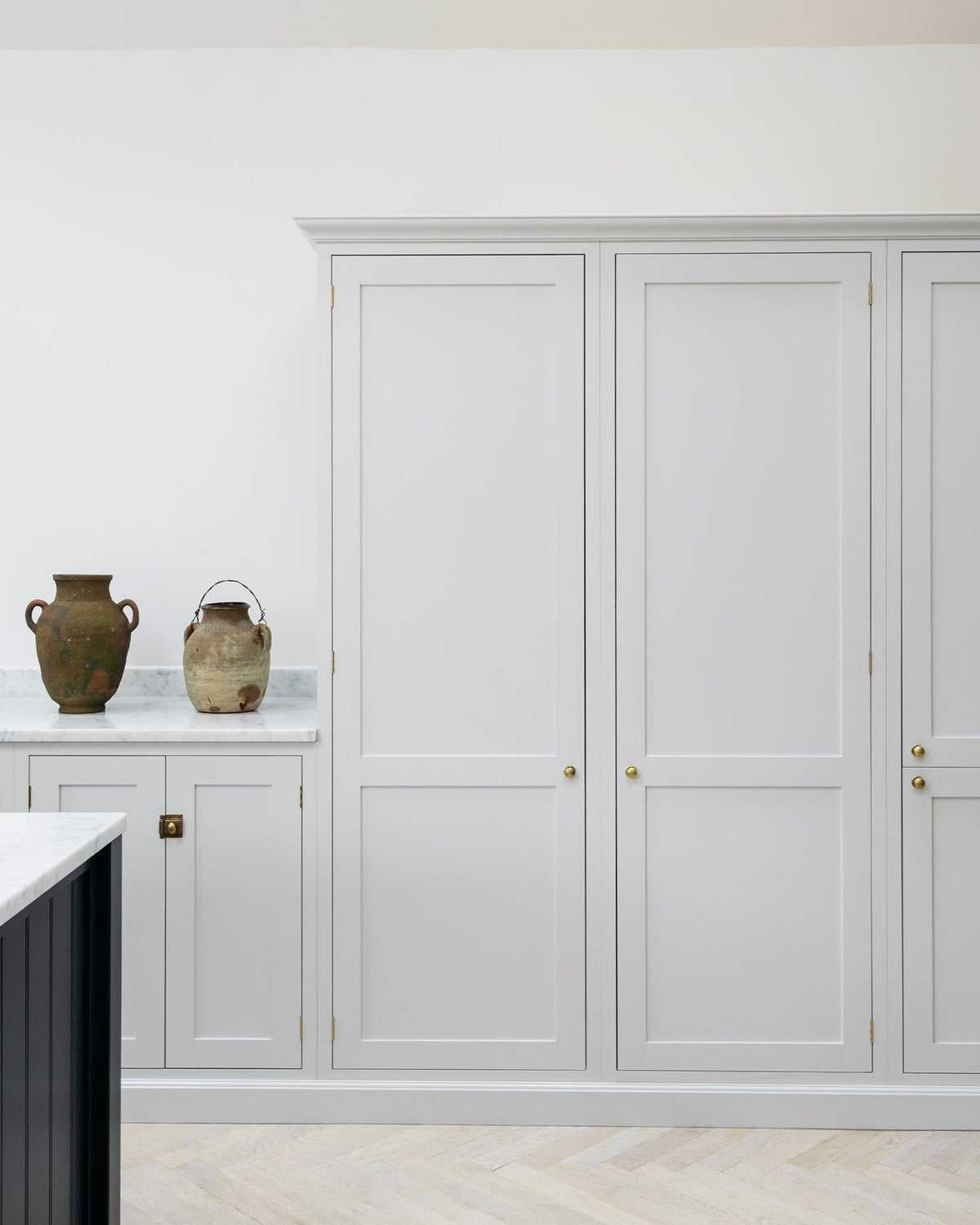 A straight-on view of a simple Shaker-style kitchen with off-white painted tall pantry cupboards and white walls. TEST