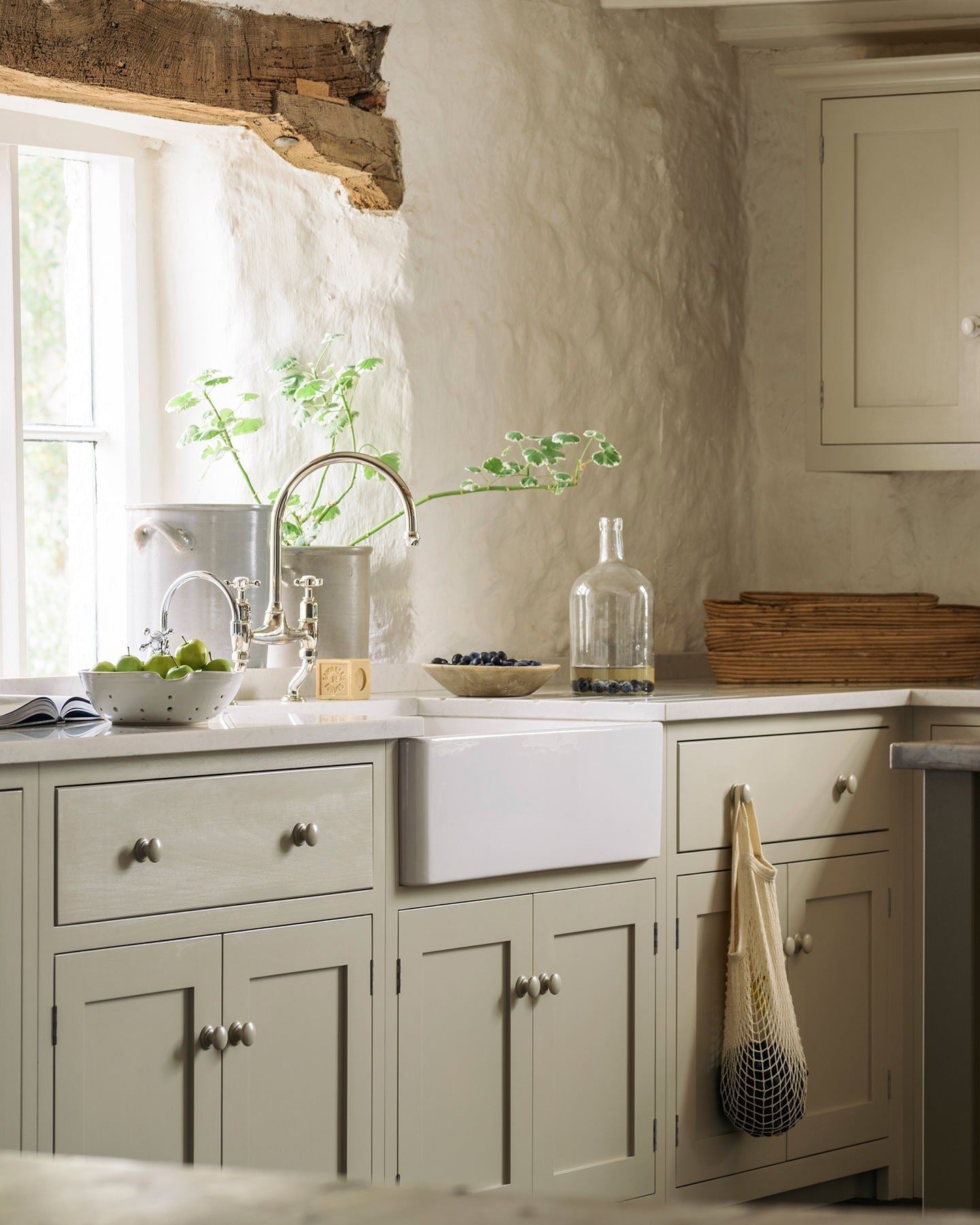 An oblique view of a Shaker-style kitchen sink cupboard, painted in a creamy mushroom colour and paired with chrome taps and a white ceramic Belfast sink.