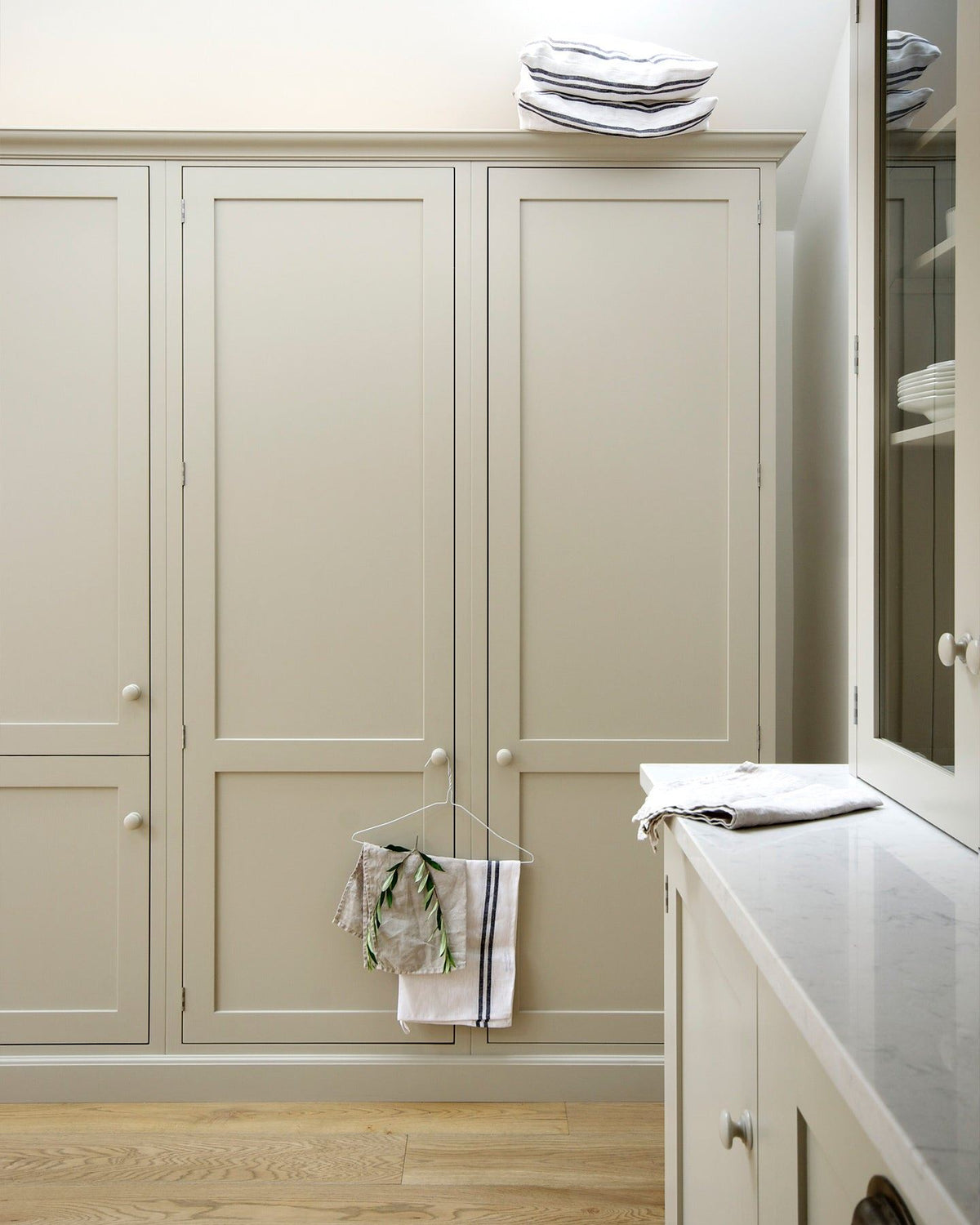 A straight-on view of simple Shaker-style tall pantry cupboards painted in a creamy mushroom colour. TEST