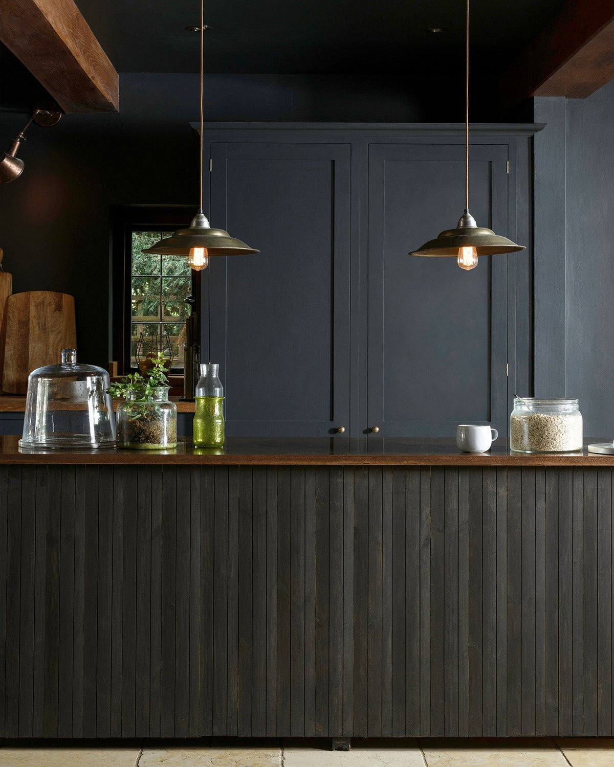 A moody kitchen with dark blue painted ceiling, walls and kitchen pantry cupboard with a vintage slatted island with an aged copper worktop in the middle of the room. TEST