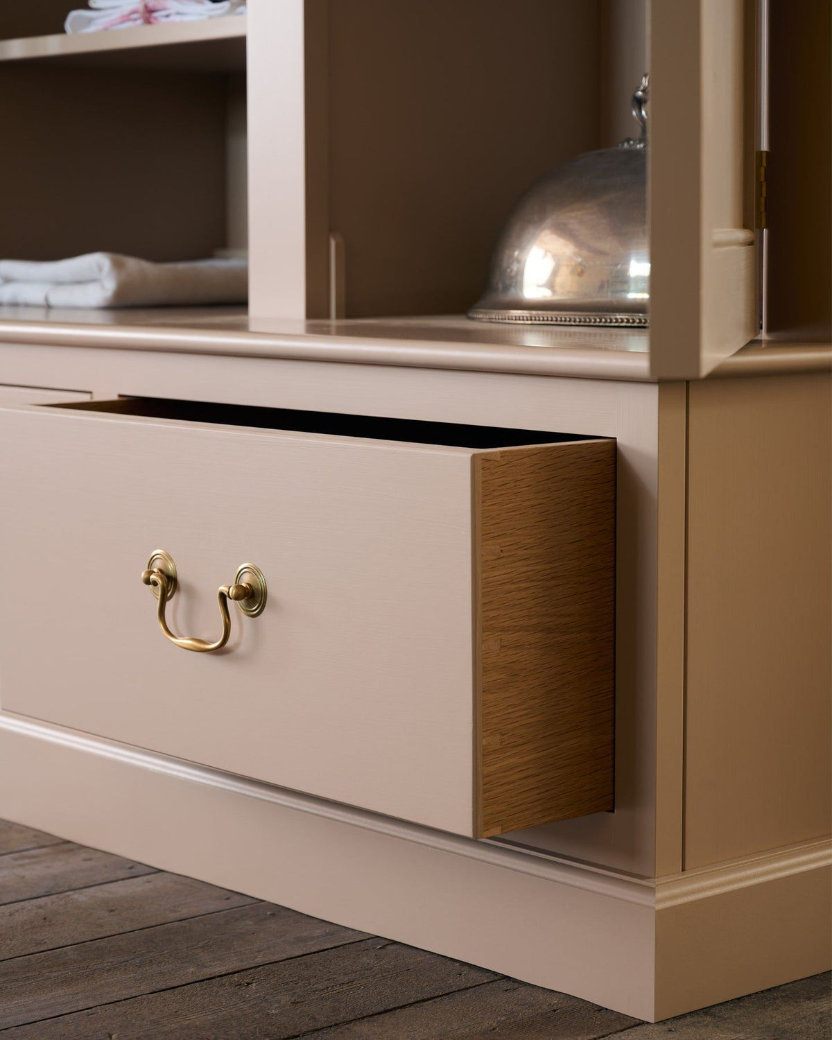 A close-up oblique view of a soft pink coloured oak drawer box with dovetailed joinery and a Georgian-style swing handle in a tarnished silver finish. TEST