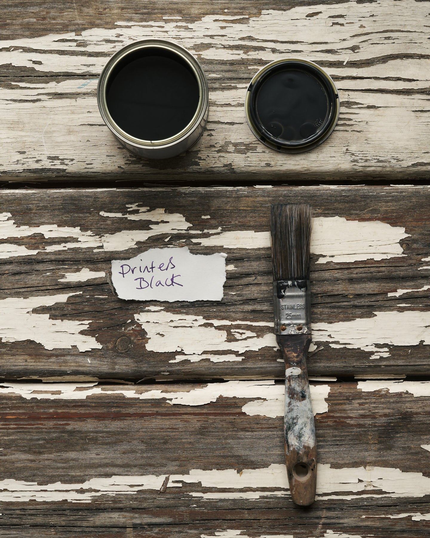 An overhead view of an open paint pot and a worn brush on a rustic tabletop. The black colour inside is labelled 'Printer's Black'.
