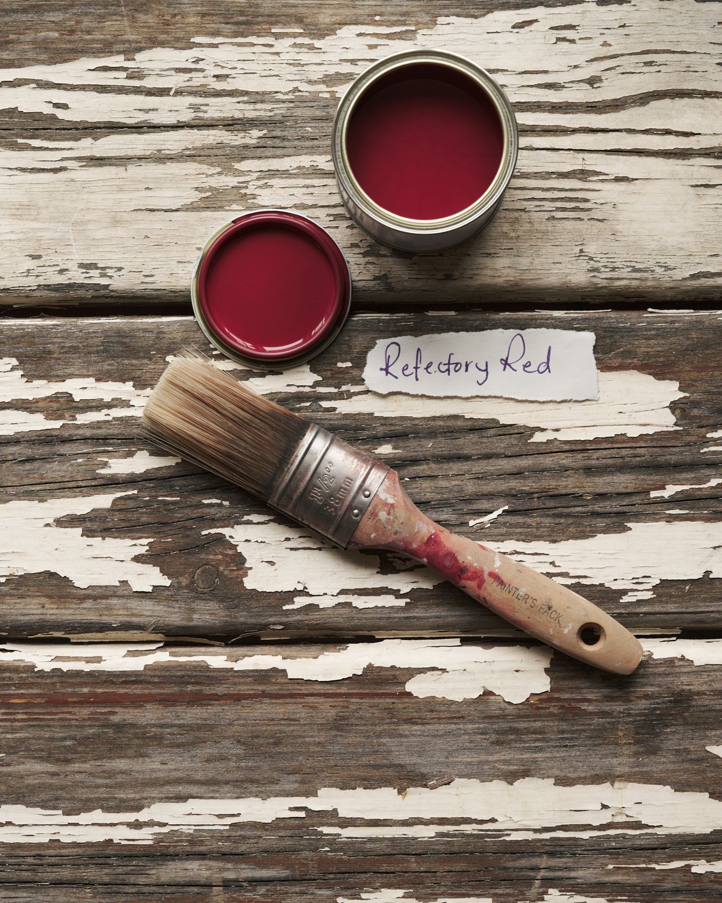 An overhead view of an open paint pot and a worn brush on a rustic tabletop. The rich red colour inside is labelled 'Refectory Red'.