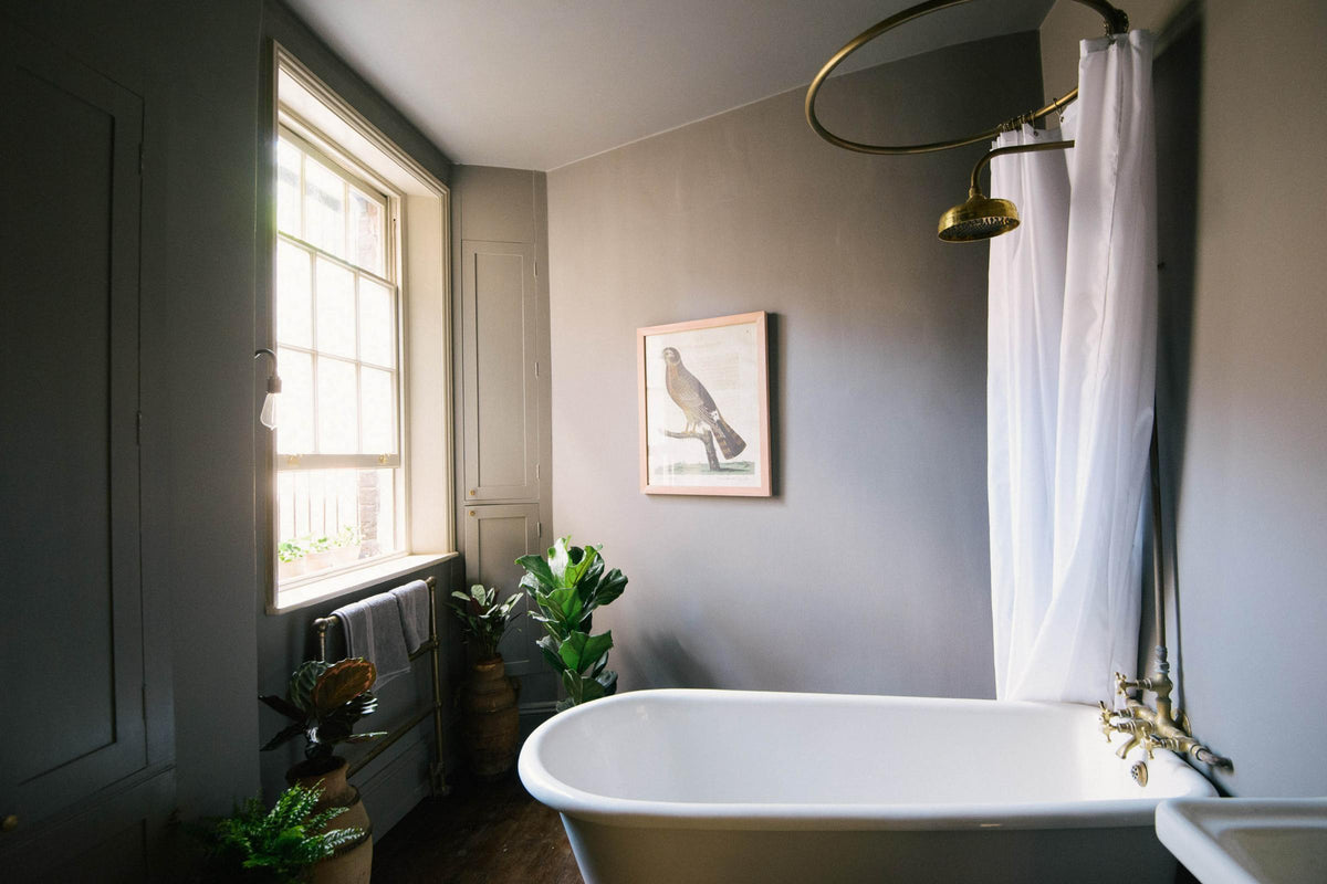 A dramatic image of a muted grey bathroom with a beautiful bathtub with a ring curtain.